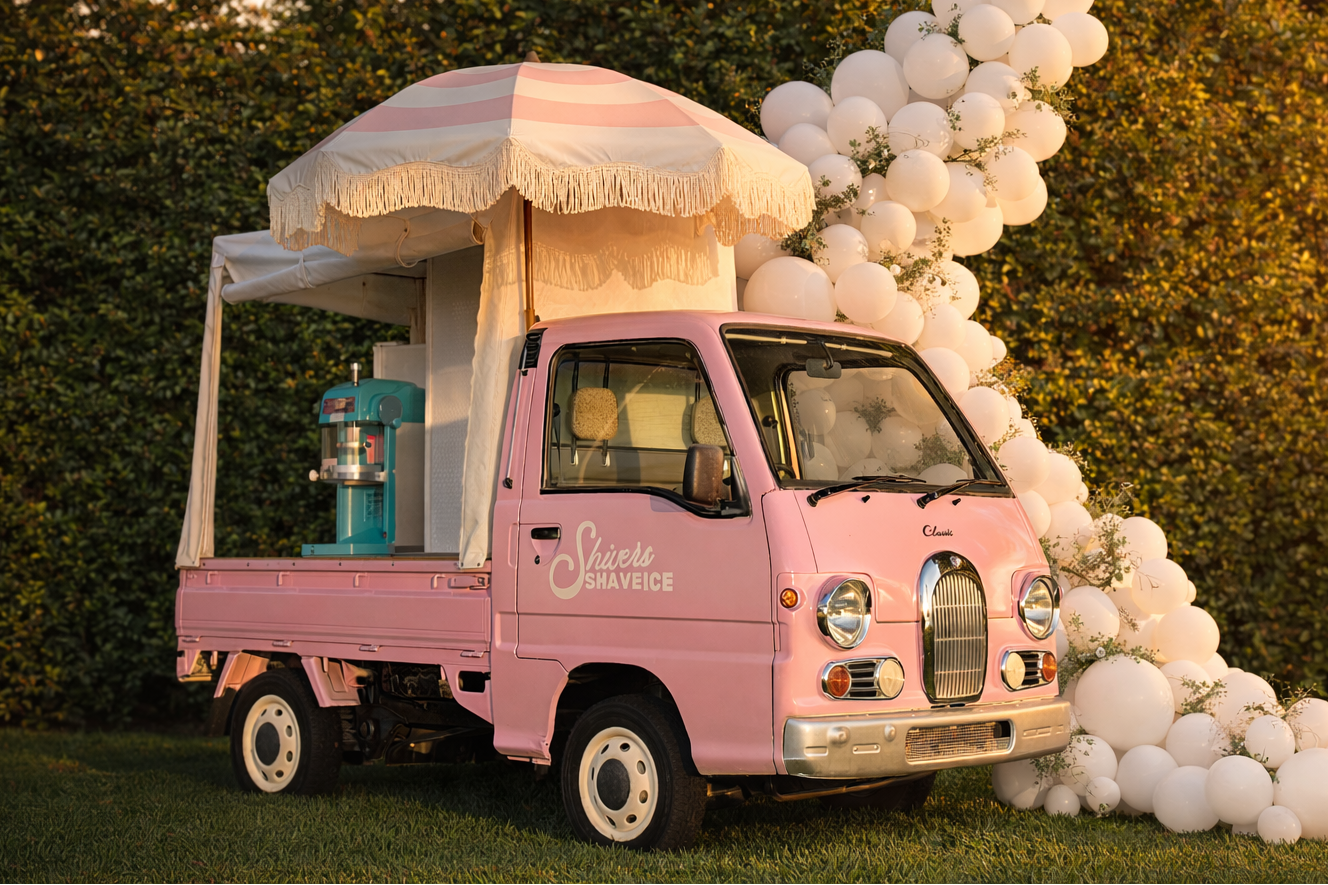 Pink classic-style shave ice truck with decorative balloons in a garden setting